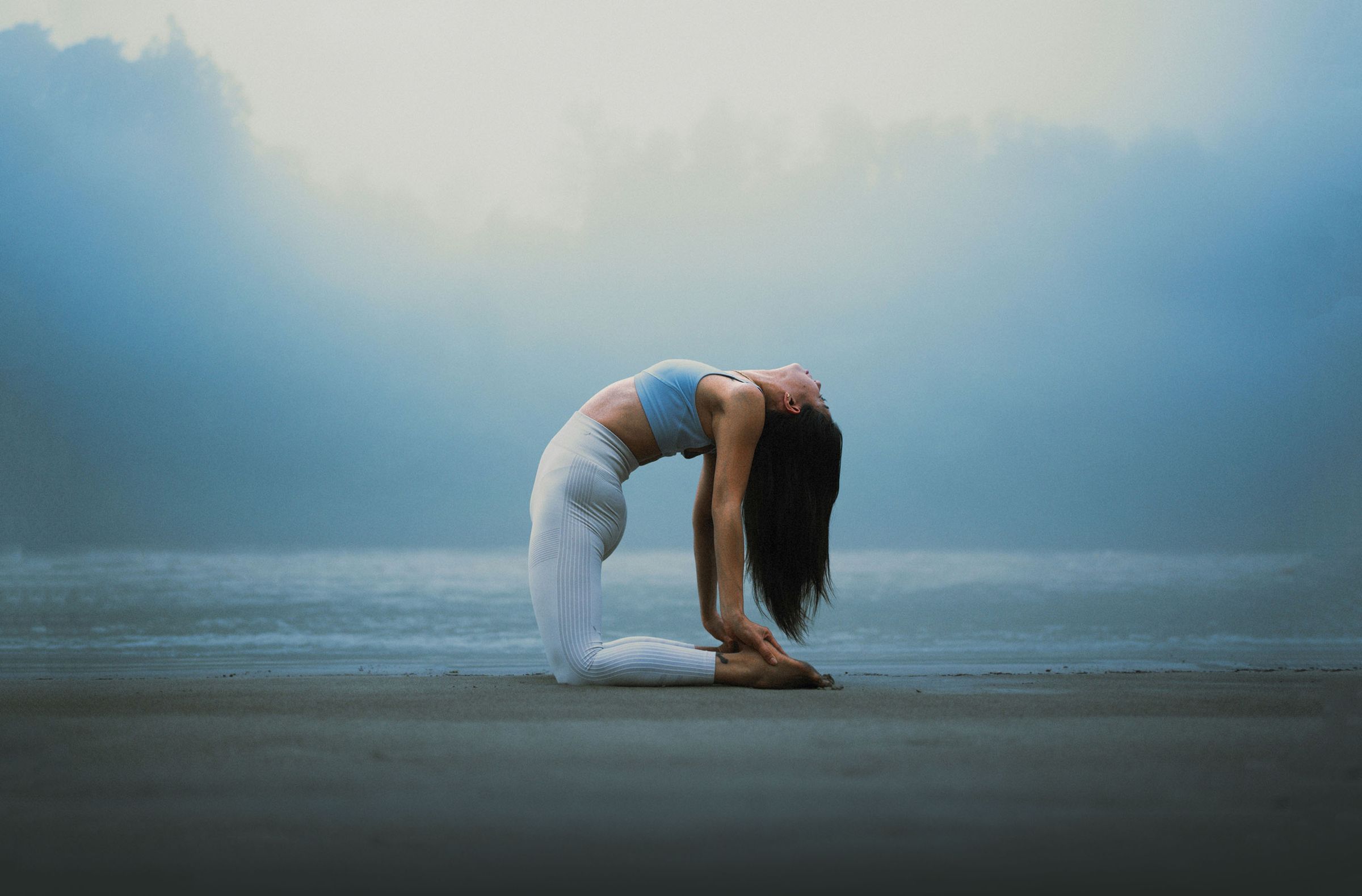 Frau in einer Yoga-Rückbeuge am nebligen Strand